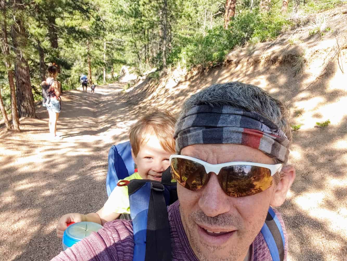 Matt taking a selfie on a forest trail with a child riding in a backpack carrier